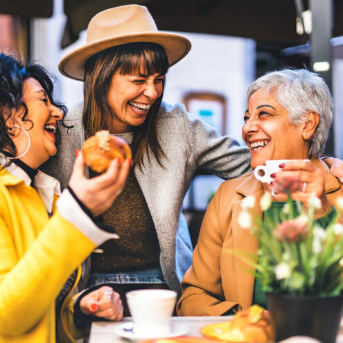 Happy three senior women enjoying breakfast eating croissant and drinking coffee at city bar cafeteria